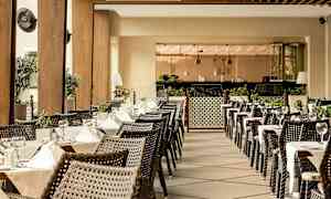 Uteservering med dekkede bord og kurvstoler, omgitt av grøntområder og moderne interiør. (AI-generert tekst)