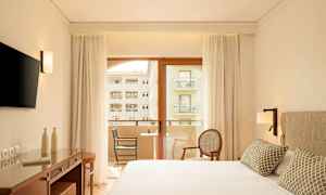 Moderne hotellrom med dobbeltseng, skrivebord, TV og balkong med utsikt. (AI-generert tekst)