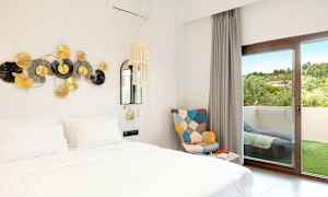 Bilde av et hotellrom med en hvit seng, dekor på veggen og en dør til en balkong. (AI-generert tekst)