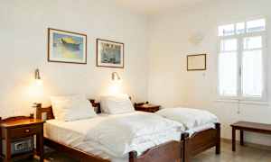 Et soverom med to enkeltsenger, hvite vegger og malerier på veggen. (AI-generert tekst)