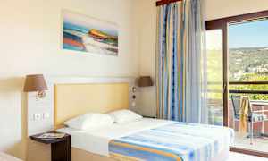 Et hotellrom med en seng, opplyst med naturlig lys fra en balkong. (AI-generert tekst)