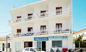 Hvit bygning med skilt for hotell og utleie av kjøretøy. Mopeder og en bil er parkert foran. (AI-generert tekst)