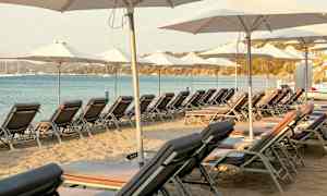 Solstoler og parasoller plassert på sandstrand ved sjøen. (AI-generert tekst)