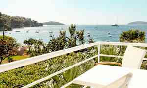 Utsikt fra en balkong over havet med båter og vegetasjon. (AI-generert tekst)