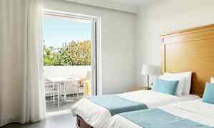 Hotellrom med to enkeltsenger, blå sengetøy og direkte tilgang til en balkong med trær i bakgrunnen. (AI-generert tekst)