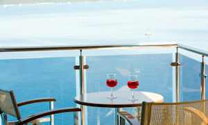 To glass med rød drikk på et bord på en balkong med utsikt over havet. (AI-generert tekst)