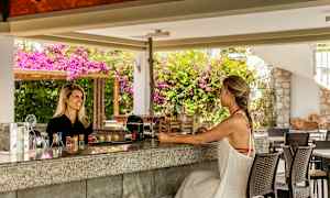 En utendørsbar med to personer, fargerike drikker og planter i bakgrunnen. (AI-generert tekst)