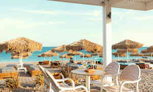 Utsikt over en sandstrand med parasoller og solsenger, sett fra en sitteplass med bord og stoler. (AI-generert tekst)