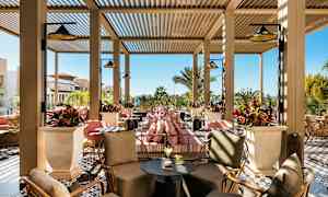 Utendørs loungeområde med sitteplasser og planter, med solfylt vær i bakgrunnen. (AI-generert tekst)