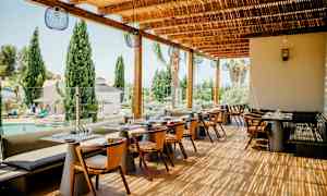 Restaurant utendørsterrasse med bord og stoler, med utsikt over et basseng og trær. (AI-generert tekst)