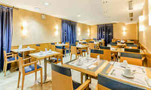 Et spisesal med oppsatte bord og stoler, vegger i varme toner og blå gardiner. (AI-generert tekst)