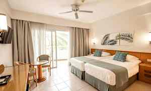 Hotellrom med to senger, sittegruppe og balkong. (AI-generert tekst)