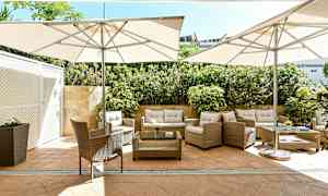 Utemøbler med parasoller på en terrasse belagt med stein og omgitt av grøntområder. (AI-generert tekst)