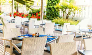 Utendørs servering med hvite flettede stoler og dekkede bord med blå bordbrikker. (AI-generert tekst)