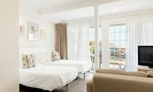 Et lyst hotellrom med to enkeltsenger, store vinduer og havutsikt. (AI-generert tekst)