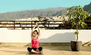 Person sitter i yogastilling på en terrasse med utsikt over byen og fjellene. (AI-generert tekst)