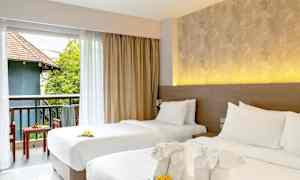 To oppredde enkeltsenger med dekorative håndklær og blomster. Utsikt mot en møblert balkong med grønt og bygning. (AI-generert tekst)