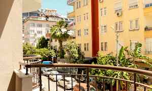 Utsikt fra en balkong mot en gate omgitt av bygninger og grønne områder. (AI-generert tekst)