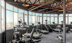 Lyse treningsstudio med treningsmaskiner og utsikt gjennom store vinduer. (AI-generert tekst)