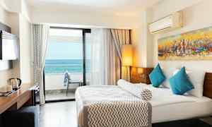 Hotellrom med en stor seng, blå puter og havutsikt fra balkongen. (AI-generert tekst)