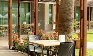 En uteplass med bord, stoler og blomster foran en bygning med glassvinduer. (AI-generert tekst)