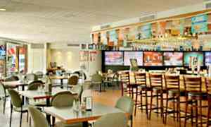 En interiør av en restaurant med bord og stoler samt en bardisk med høye stoler. (AI-generert tekst)