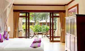 Hotellrom med en oppredd seng foran glassdører som åpner ut mot en grønn hage. (AI-generert tekst)