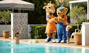 To maskotfigurer, en giraff og en bjørn, står ved utendørsbassenget. (AI-generert tekst)