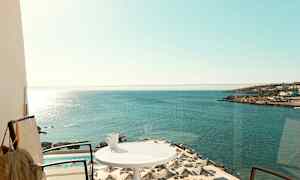 En balkong med utsikt over havet, parasoller ved et basseng og en kopp på et bord. (AI-generert tekst)