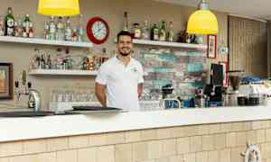 En bar med hyller fulle av flasker og en klokke på veggen. (AI-generert tekst)