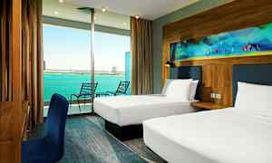 Et hotellrom med to enkeltsenger, et skrivebord med en blå stol og en balkong med utsikt over havet. (AI-generert tekst)