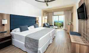 Hotellrom med to enkeltsenger, sitteområde og balkong. (AI-generert tekst)