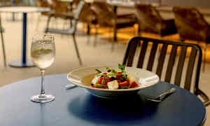 Uteservering ved havet med en tallerken salat og et glass hvitvin på et bord. (AI-generert tekst)