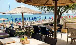 En uteservering med parasoller nær en strand med solsenger og utsikt over havet. (AI-generert tekst)