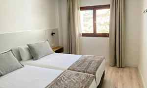 Et hotellrom med to enkeltsenger, et vindu med lysinnslipp og del av utsikten utenfor. (AI-generert tekst)