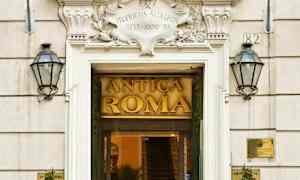 Inngang til bygning med skiltet Antica Roma, omgitt av to flagg og plantepynt. (AI-generert tekst)