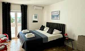 Et soverom med en dobbeltseng, sittemøbler og en glassdør ut mot en balkong. (AI-generert tekst)