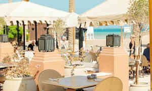 Utendørs servering med bord og stoler under parasoller nær stranden. (AI-generert tekst)