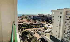 Utsikt fra en balkong over et byområde med havet i bakgrunnen, og solfylt vær. (AI-generert tekst)