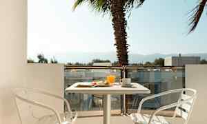 En balkong med et bord, to hvite stoler og frokost servert. En palme er synlig i bakgrunnen. (AI-generert tekst)