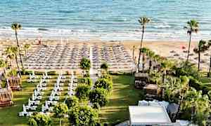 Bilde av en strand med solsenger og parasoller samt et grøntområde med skyggegivende tak foran. (AI-generert tekst)