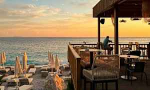 En solnedgang ved havet med en restaurantterrasse og solsenger på stranden. (AI-generert tekst)