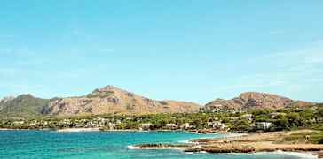 Kystlinje med klart blått vann og fjell i bakgrunnen. (AI-generert tekst)