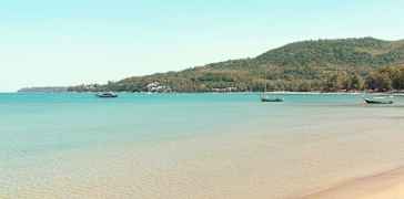 En strand med klart vann og båter lenger ute på sjøen. (AI-generert tekst)