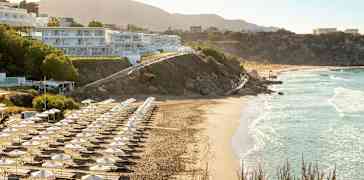 Strand med solsenger og parasoller, bygninger på skråningen. (AI-generert tekst)
