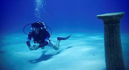En dykker under vann nær en antikk søyle på havbunnen. (AI-generert tekst)