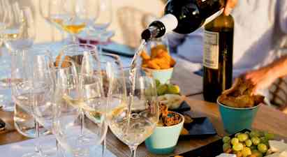 Et bord med glass fylt med hvitvin som serveres, omgitt av ulike snacks som ost, brød og frukt. (AI-generert tekst)