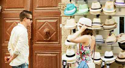 En person prøver en hatt ved et salgsbord med ulike hatter. (AI-generert tekst)