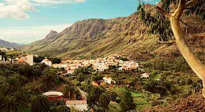 En fjelllandsby med hvite hus og rødt tak plassert i en grønn dal omgitt av høye fjell. (AI-generert tekst)