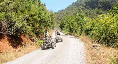 Personer kjører firehjulinger på en grusvei omgitt av grøntområder. (AI-generert tekst)